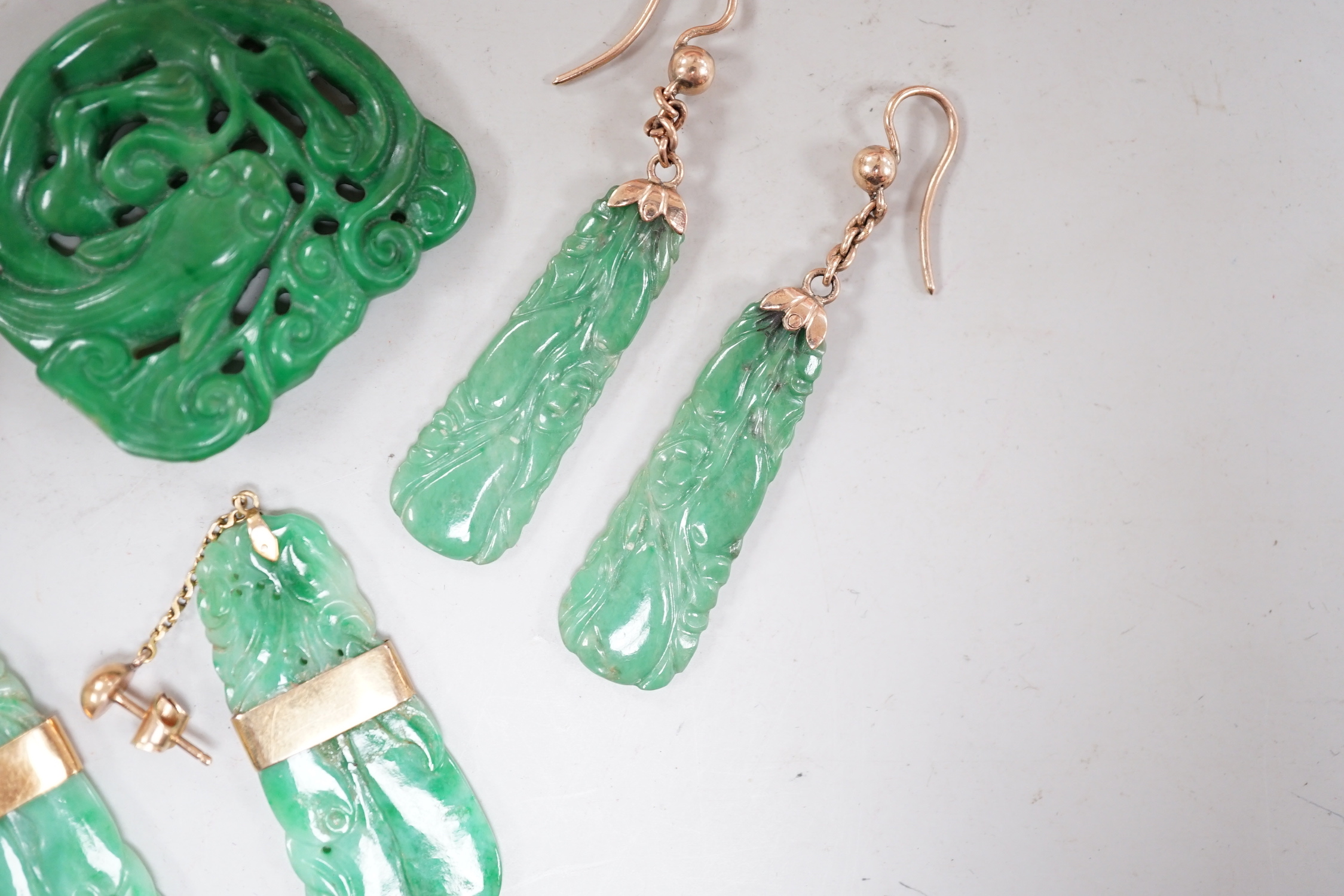 A Chinese carved hardstone pendant, 64mm, a pierced green hardstone pendant on chain and two pairs of yellow metal mounted carved jade earrings.